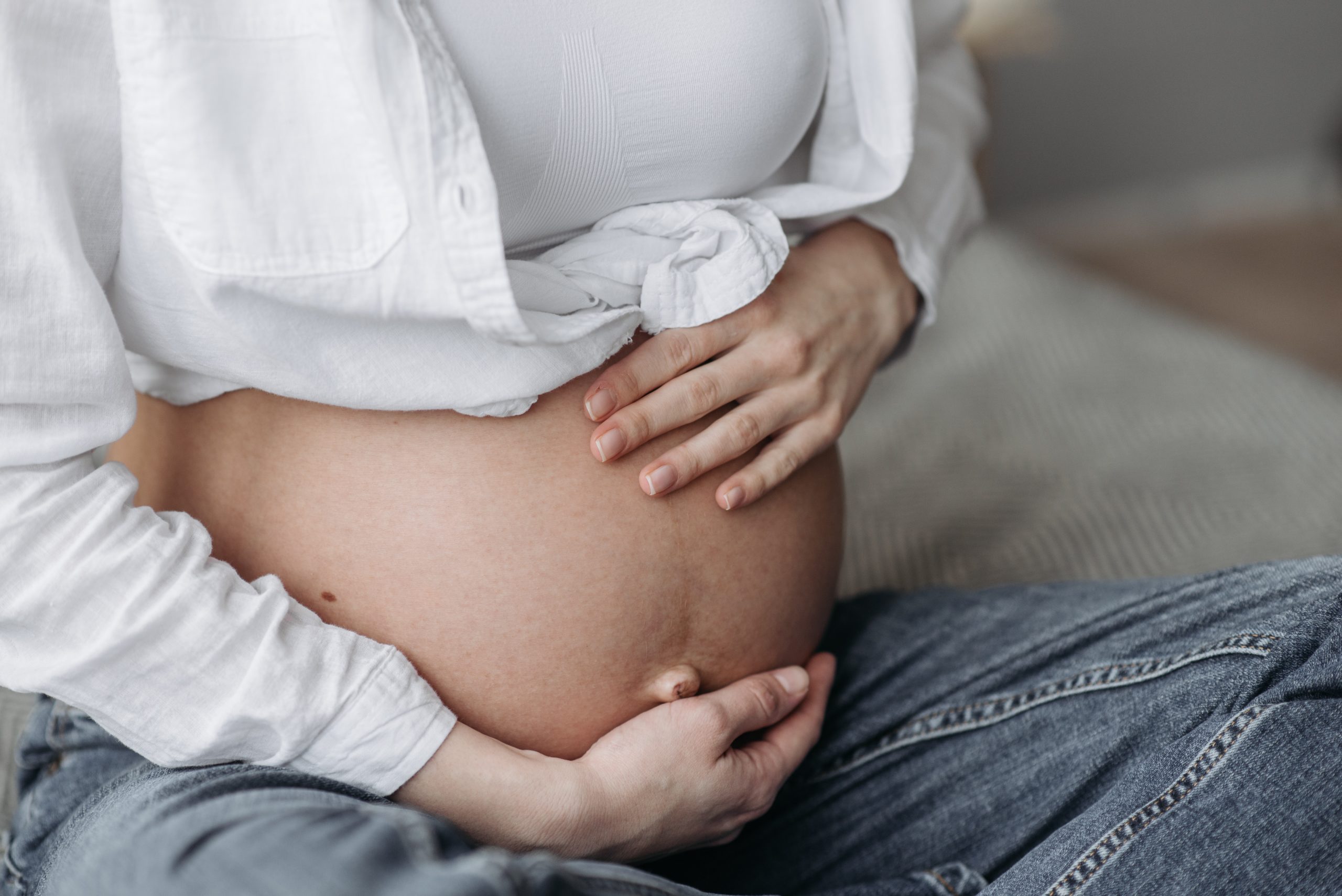 Expectant parent sitting with both hands resting on their pregnant belly